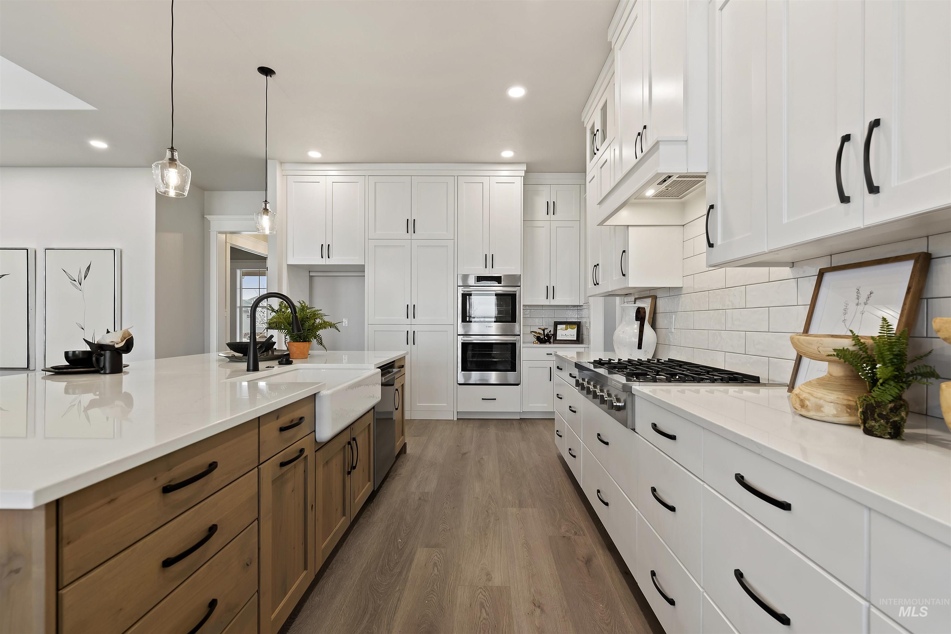 9283 Basin Kid Court Middleton, ID 83644 - Photo 4 of 21 Dual tone kitchen with two tone cabinets, dark wood-style flooring, hanging light fixtures, stainless steel appliances, and light stone counters