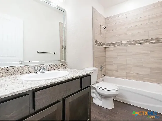 a bathroom with a granite countertop sink a toilet a mirror and bathtub
