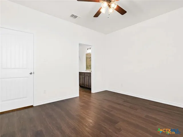 an empty room with wooden floor chandelier fan and windows
