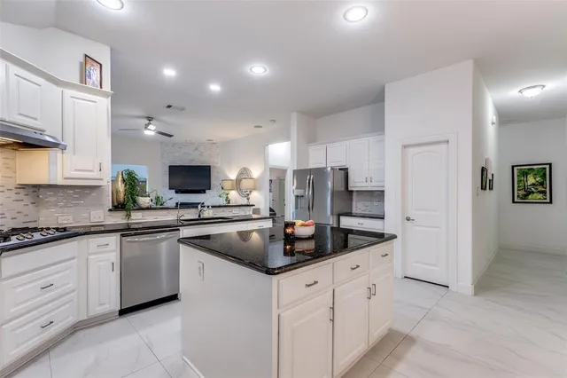 a kitchen with stainless steel appliances granite countertop a sink a refrigerator and white cabinets