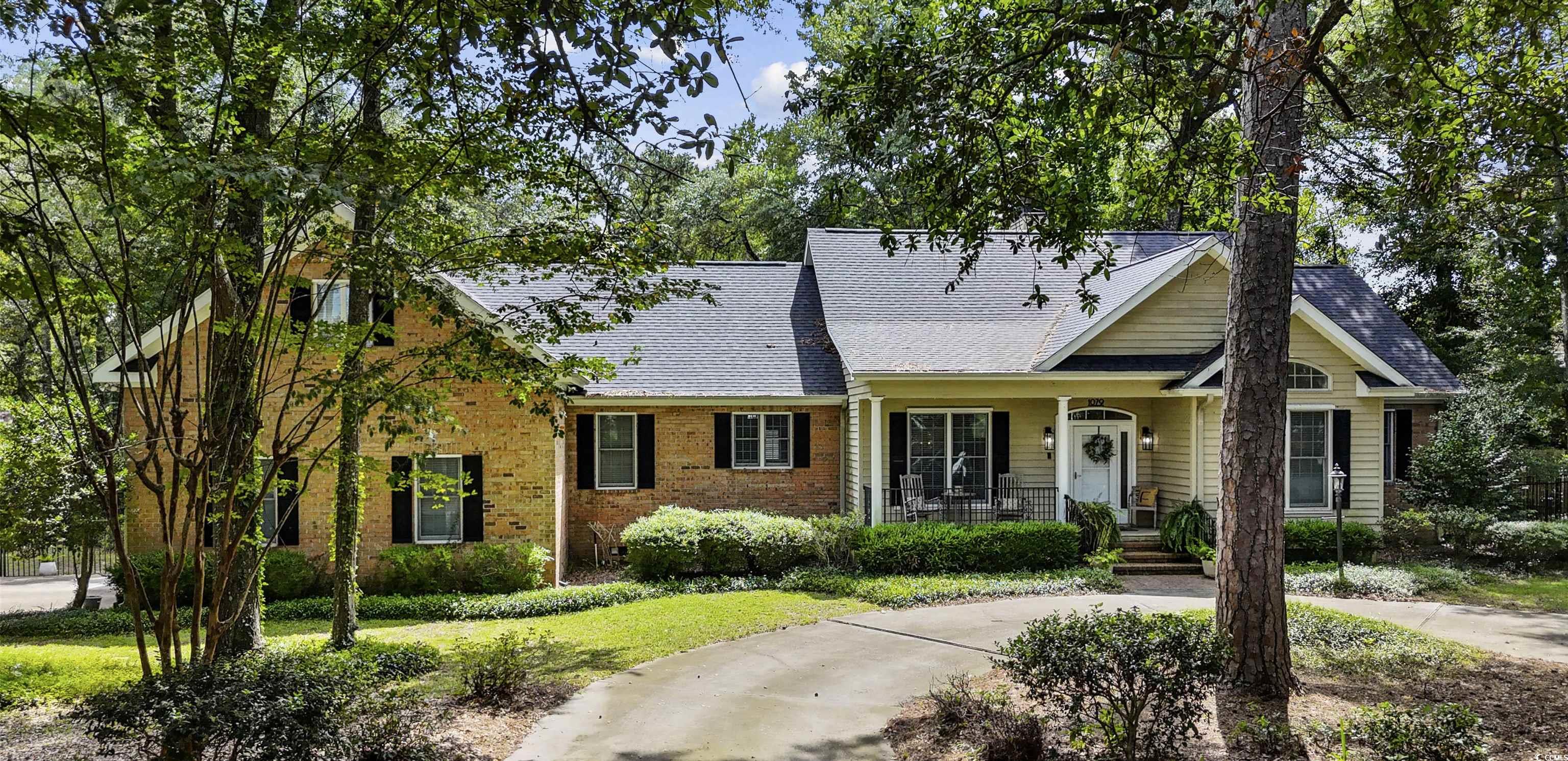 View of front of property with a porch, brick siding, a front lawn, and roof with shingles