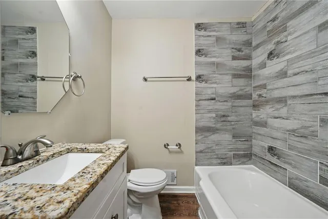 a bathroom with a granite countertop bathtub sink vanity mirror and toilet