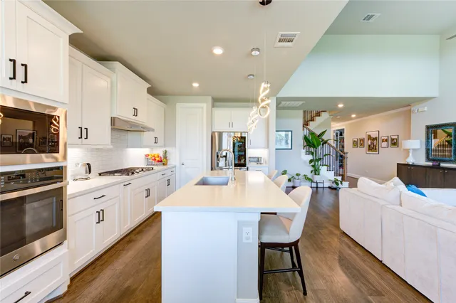 a kitchen with stainless steel appliances kitchen island granite countertop a stove a sink a refrigerator and white cabinets with wooden floor