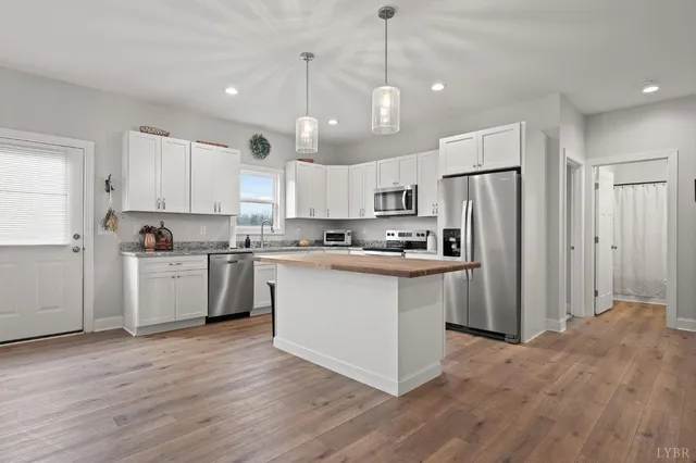 a kitchen with stainless steel appliances granite countertop a refrigerator a sink dishwasher a stove and white cabinets with wooden floor