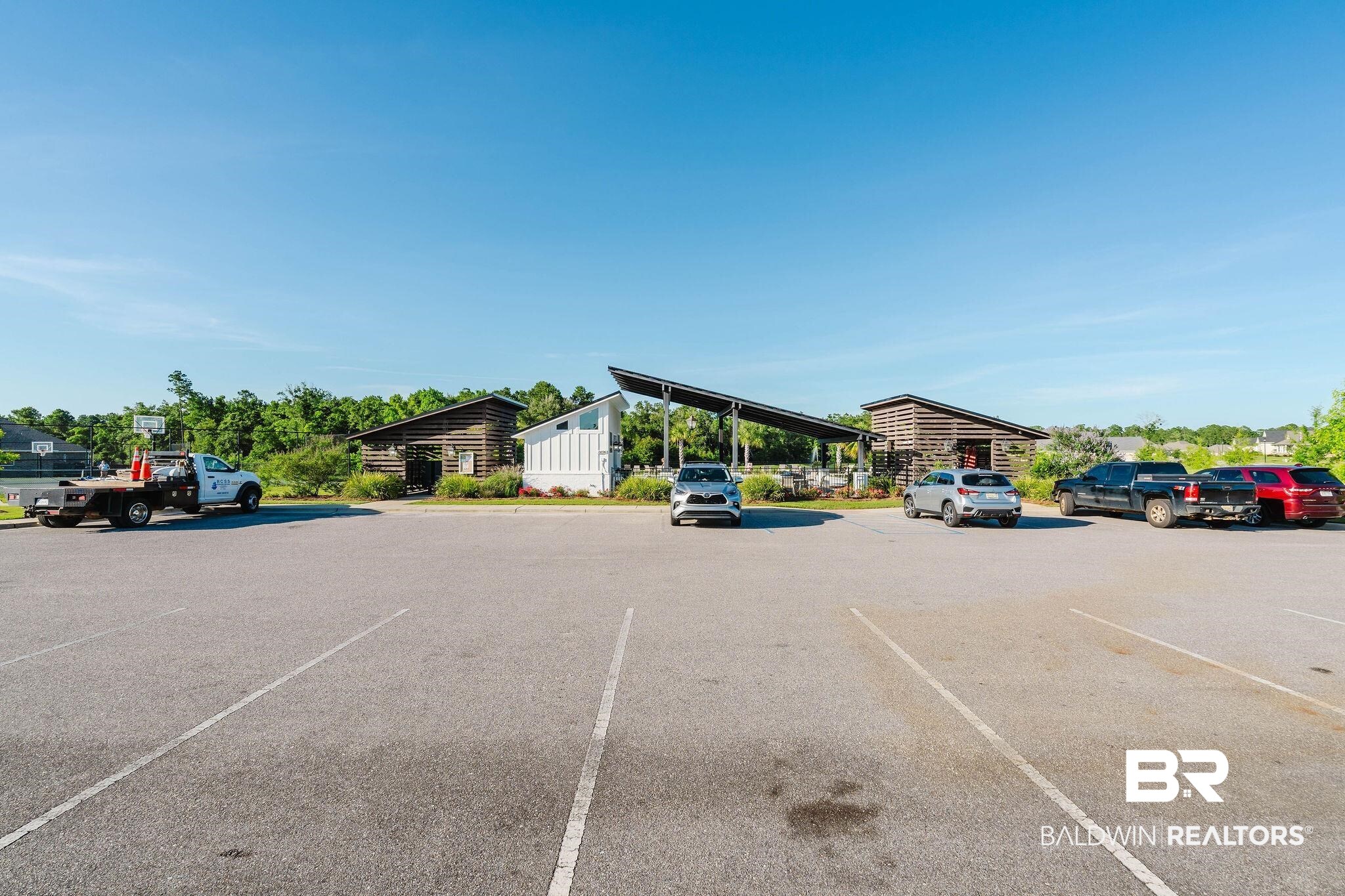 7872 Calverton Street Foley, AL 36535 - Photo 65 of 76 Paved parking area with marked spaces, bordered by established landscaping and architectural structures featuring wood siding and modern roof lines