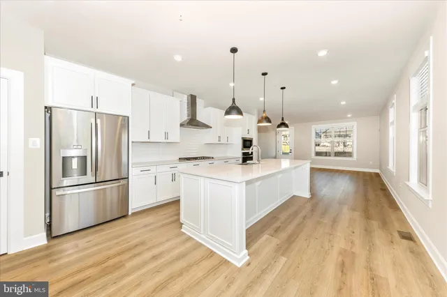 a large kitchen with kitchen island a stove a sink dishwasher a refrigerator white cabinets and wooden floor next to a window