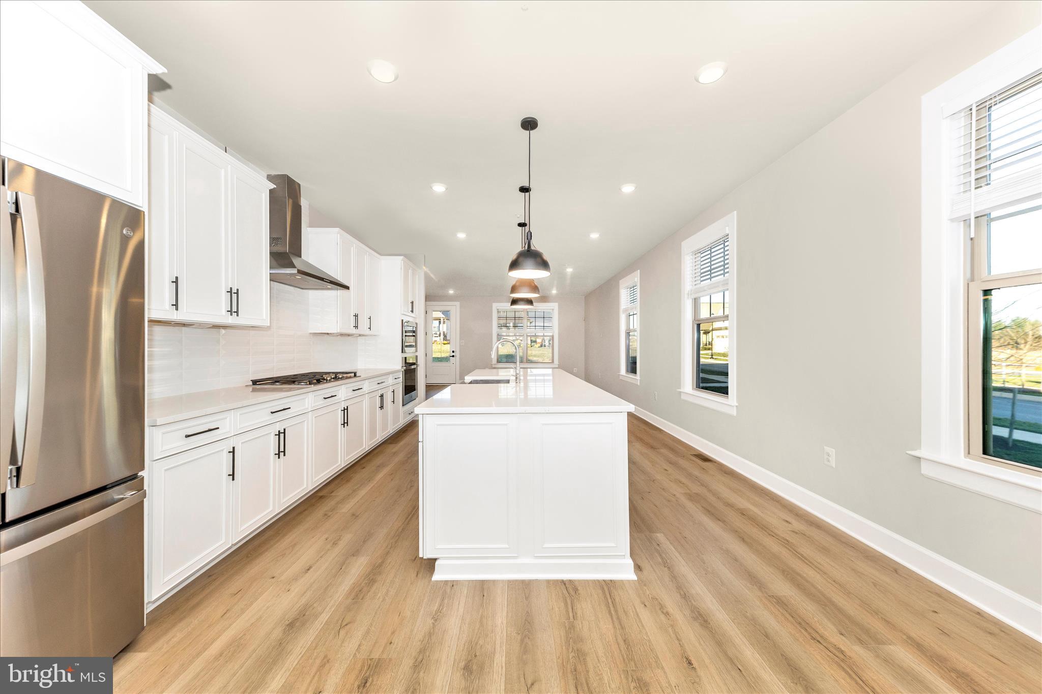 413 Bucklebury Lane Frederick, MD 21702 - Photo 15 of 58 a large kitchen with kitchen island a stove a sink dishwasher a refrigerator white cabinets and wooden floor next to a window
