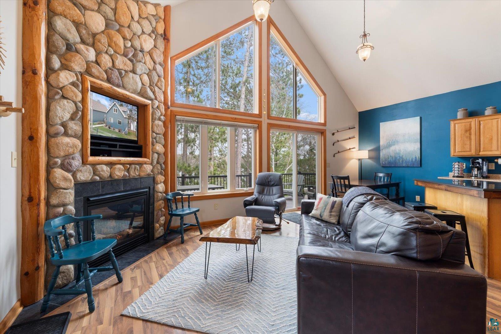 6266 Giants Ridge Road Biwabik, MN 55705 - Photo 8 of 37 Vaulted living space featuring a floor-to-ceiling stone fireplace, expansive windows, wood-finish flooring, a built-in media niche, and a kitchen pass-through with a breakfast bar