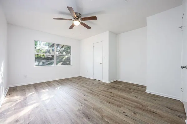 an empty room with wooden floor ceiling fan and windows