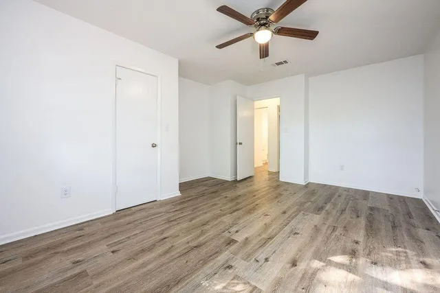 an empty room with wooden floor ceiling fan and windows
