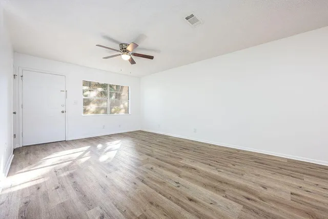 an empty room with wooden floor ceiling fan and windows
