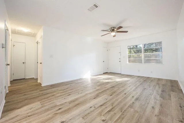 an empty room with wooden floor ceiling fan and windows