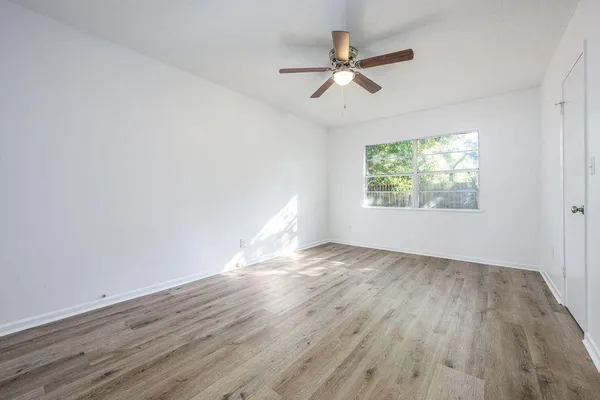 an empty room with wooden floor fan and windows