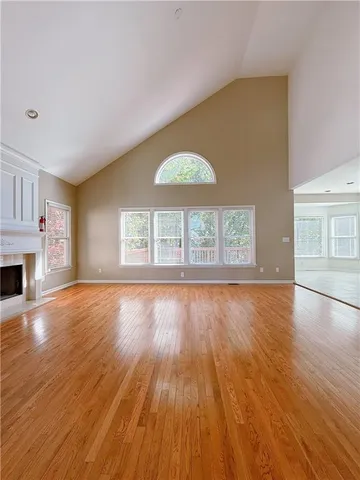 an empty room with wooden floor fireplace and windows