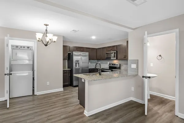 a kitchen with stainless steel appliances granite countertop a refrigerator a stove a sink and white cabinets with wooden floor