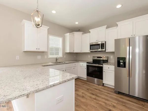 a kitchen with granite countertop a refrigerator a sink dishwasher a stove top oven a kitchen island with wooden floor and cabinets