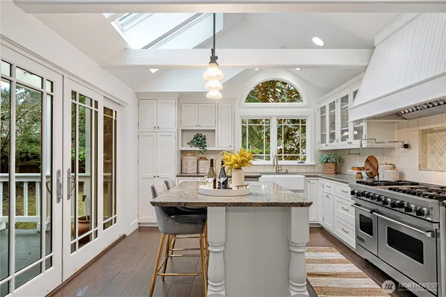 a kitchen with stainless steel appliances granite countertop a stove a sink dishwasher and white cabinets with wooden floor