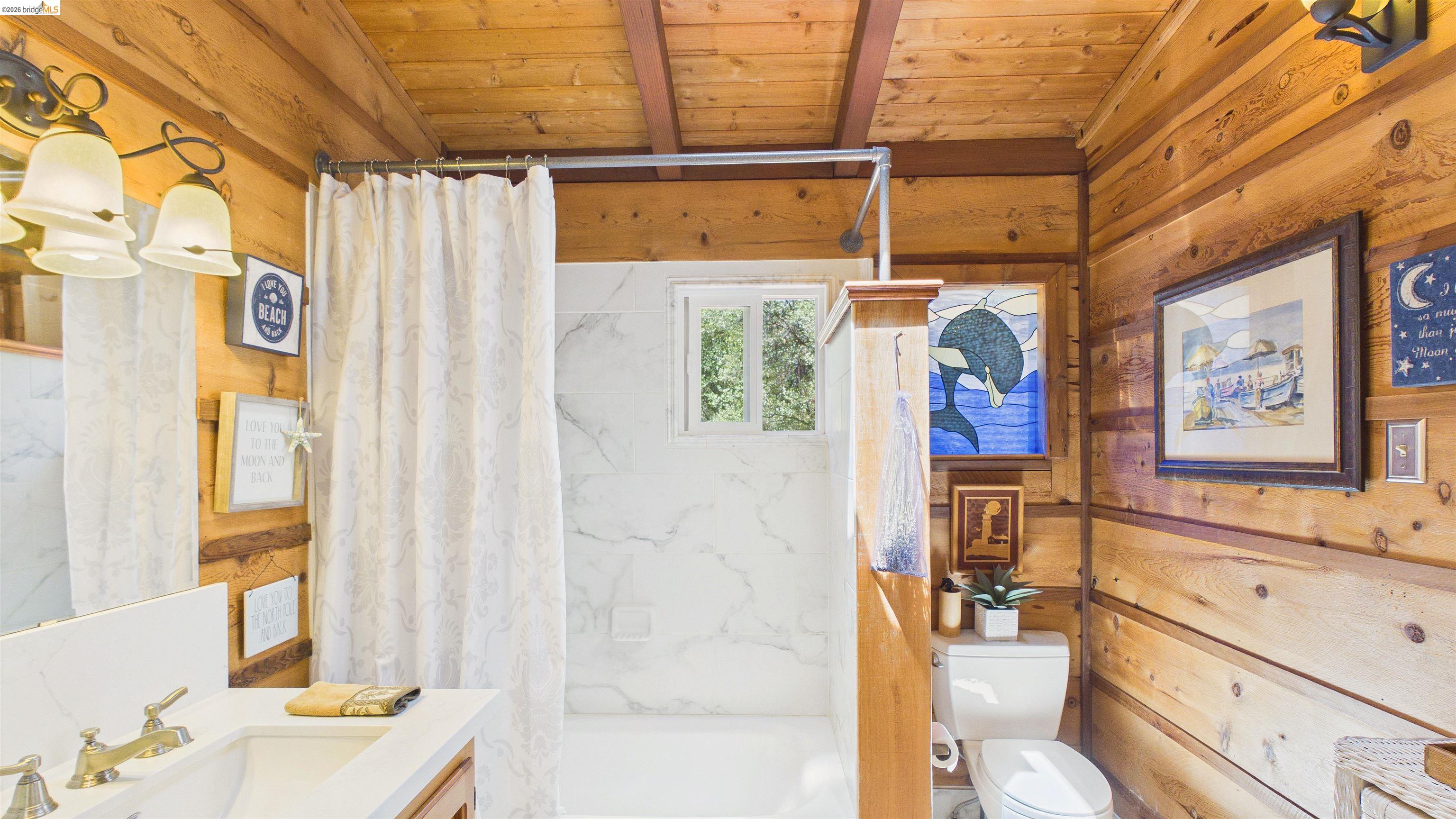 18102 Mt Eaton Road Tuolumne, CA 95379 - Photo 20 of 44 Bathroom featuring wood plank walls and ceiling, a vanity with a white countertop and dual sinks, a shower with white marble-look tiling, and a window providing natural light