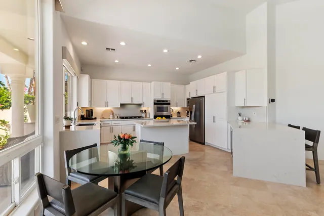a kitchen with stainless steel appliances kitchen island granite countertop a dining table chairs and refrigerator