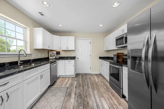 a kitchen with granite countertop a refrigerator oven a sink dishwasher and white cabinets with wooden floor