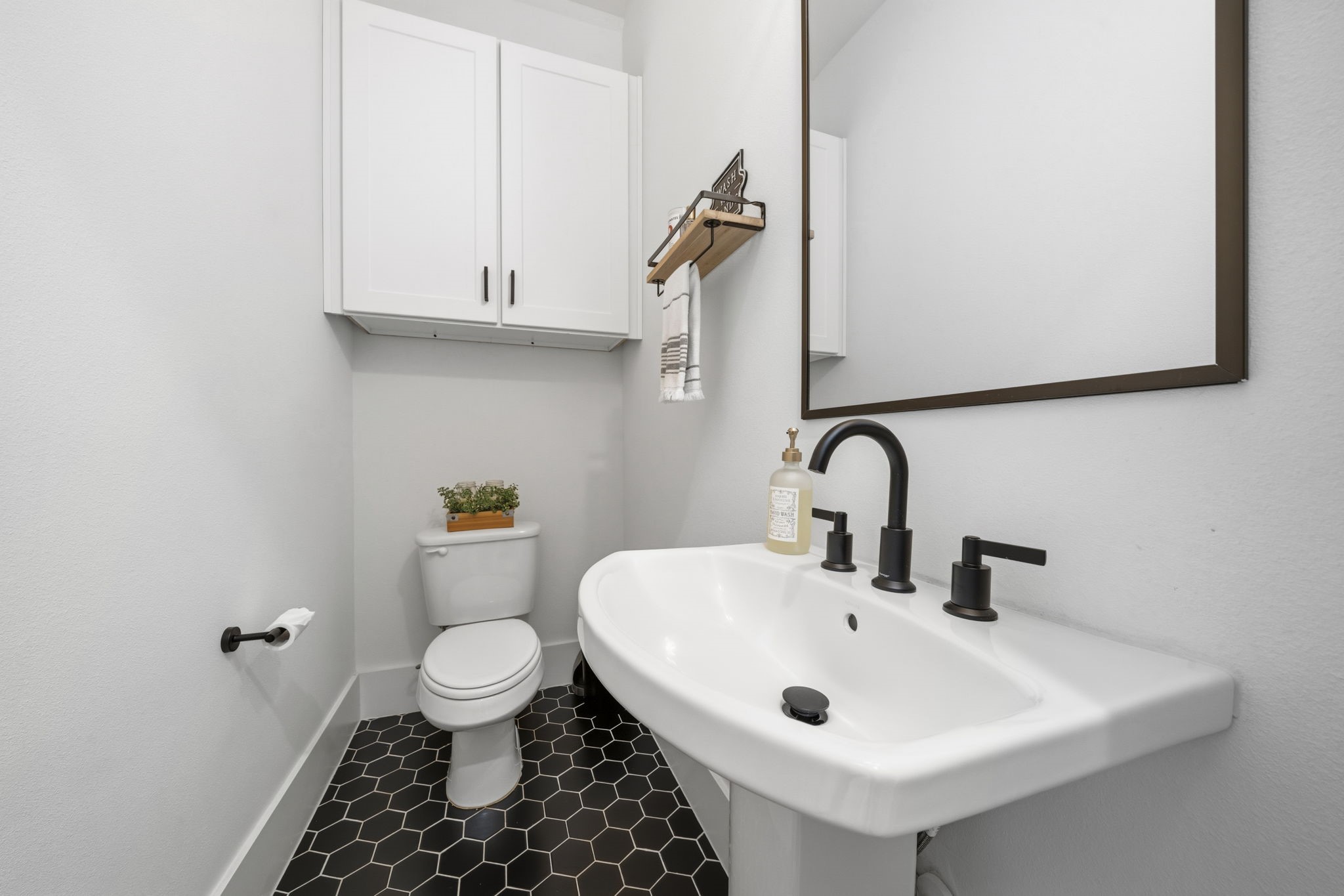 9018 Wellspring Drive Houston, TX 77080 - Photo 18 of 25 The chic guest powder room features a classic pedestal sink paired with a bold black-and-white hexagonal tile floor, creating a modern and stylish statement.