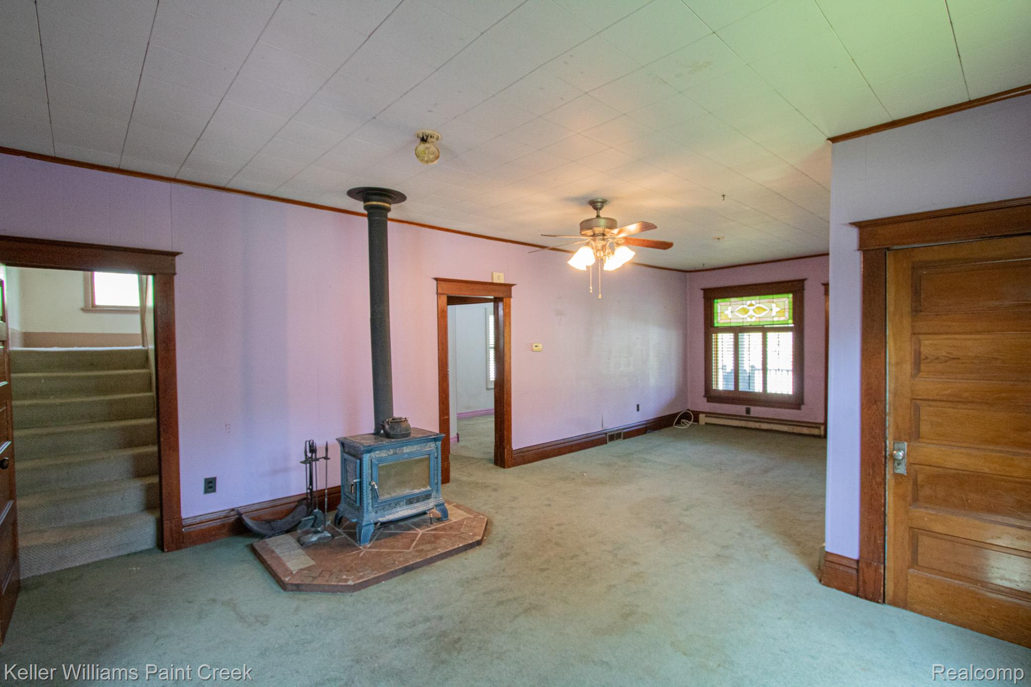 2165 Michigan Road Port Huron, MI 48060 - Photo 9 of 38 Unfurnished living room with ornamental molding, a ceiling fan, a wood stove, light carpet, and a baseboard radiator