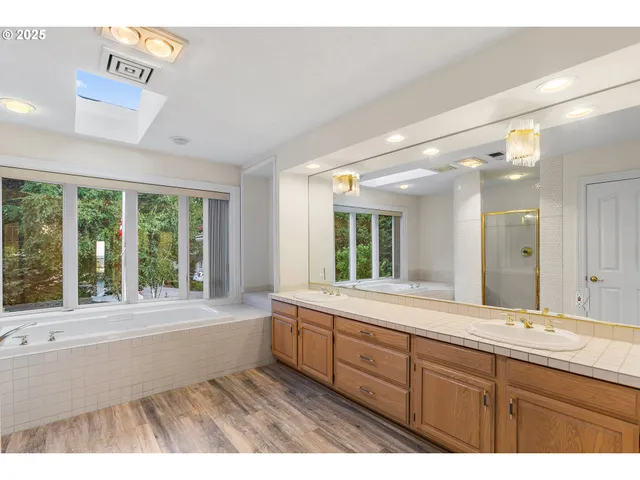 a bathroom with a sink large mirror a bathtub and next to a window