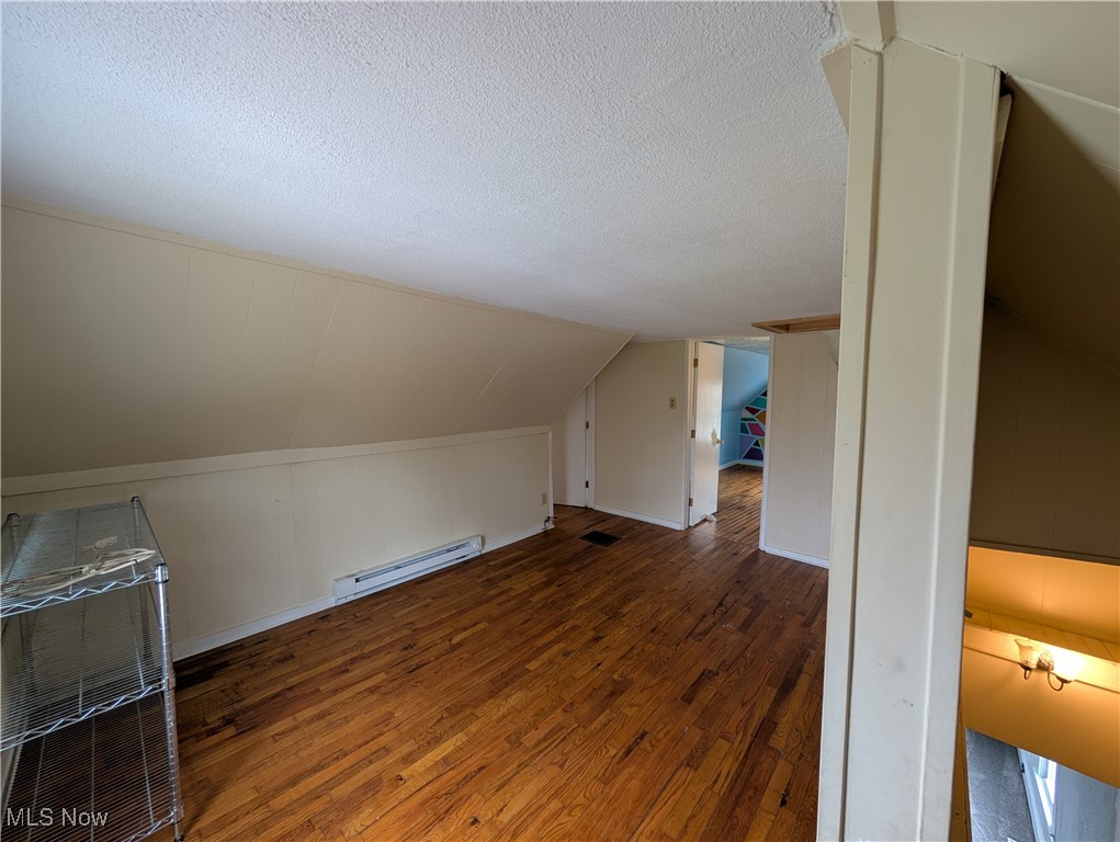 10143 Pleasant Road Pleasant City, OH 43772 - Photo 25 of 32 Additional living space with wood-type flooring, a baseboard heating unit, a textured ceiling, and vaulted ceiling