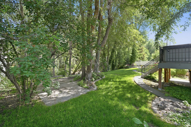 883 East 700 South Springville, UT 84663 - Photo 49 of 59 Expansive backyard featuring a manicured lawn, mature trees, a concrete pathway, a built-in fire pit, and a raised deck with metal railings