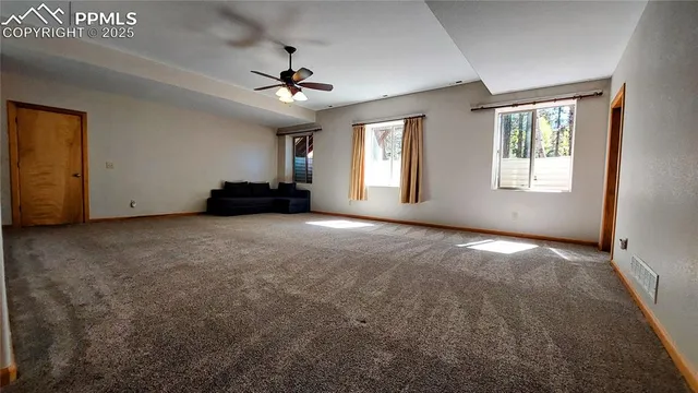 an empty room with a chandelier fan and windows