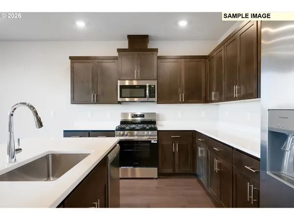 a kitchen with stainless steel appliances a sink dishwasher a stove top oven a refrigerator with wooden cabinets and a granite counter tops