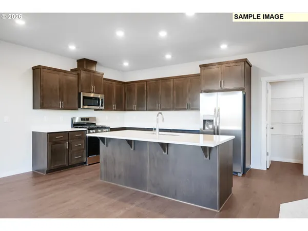 a large kitchen with stainless steel appliances a large counter top a stove a sink a refrigerator and a microwave