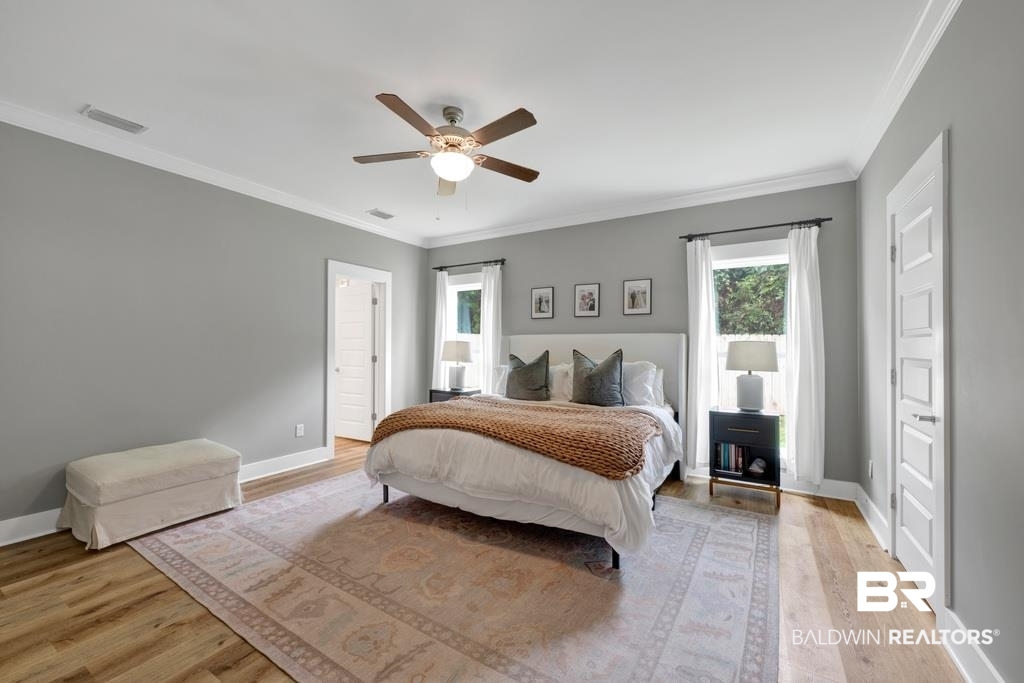 379 Pecan Ridge Boulevard Fairhope, AL 36532 - Photo 10 of 21 Spacious bedroom featuring light wood-finish flooring, a ceiling fan with integrated lighting, two windows with white trim, and a paneled door