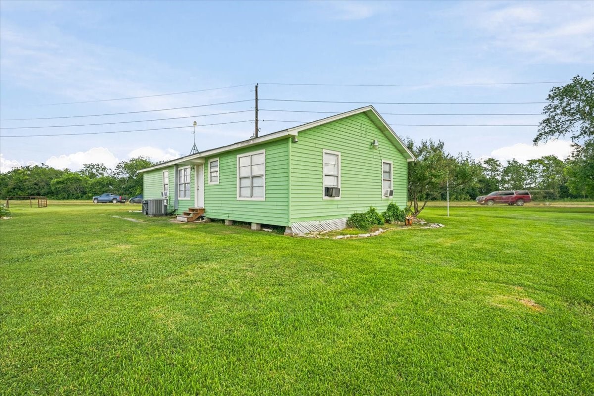 765 Norcross Road Wallis, TX 77485 - Photo 3 of 42 This photo features a charming single-story home set in a spacious, well-maintained yard. The house has a simple design with multiple windows and a small front porch. It's situated in a serene, open area with a few scattered trees and a clear sky.