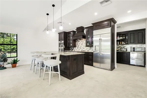 a kitchen with stainless steel appliances kitchen island granite countertop a table chairs refrigerator and sink