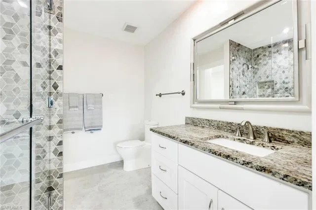 a bathroom with a granite countertop sink a toilet and shower