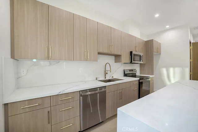 a kitchen with stainless steel appliances granite countertop a sink a stove a refrigerator and white cabinets with wooden floor