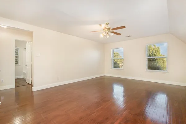 an empty room with wooden floor chandelier fan and windows