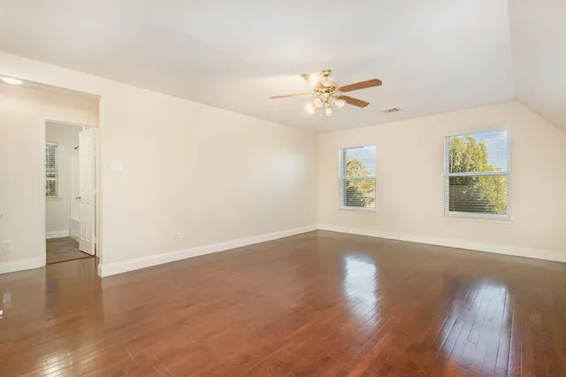an empty room with wooden floor chandelier fan and windows
