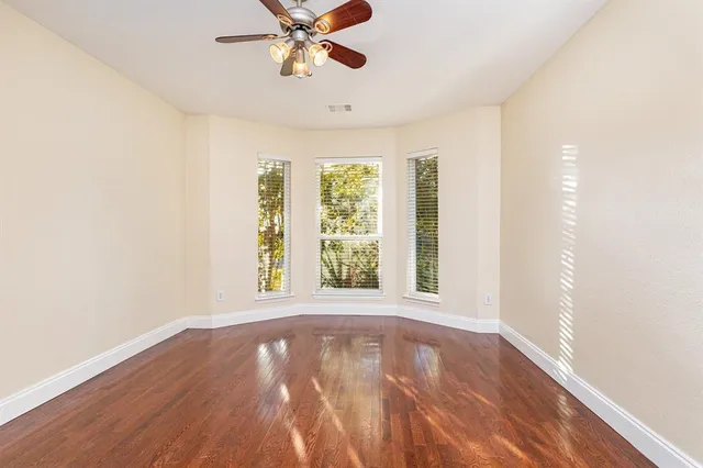 an empty room with wooden floor fan and windows