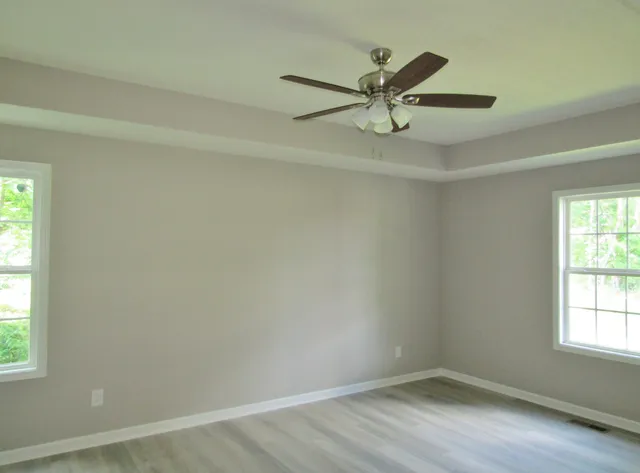 an empty room with wooden floor fan and windows