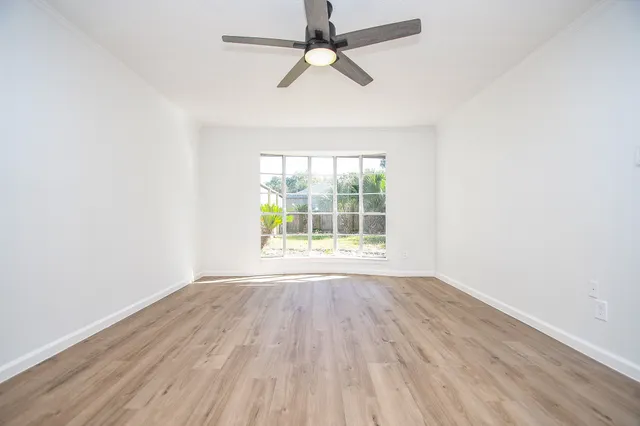an empty room with wooden floor chandelier fan and windows