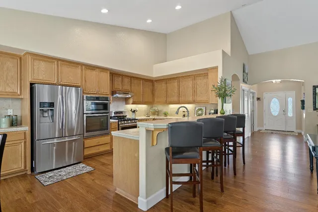 a kitchen with stainless steel appliances granite countertop a refrigerator a stove a sink a dining table and chairs with wooden floor