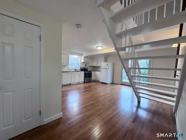 a view of empty room with wooden floor and kitchen