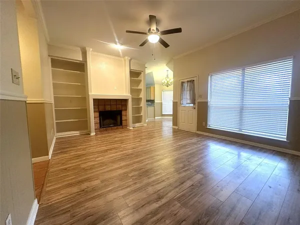 a view of an empty room with wooden floor fireplace and a window