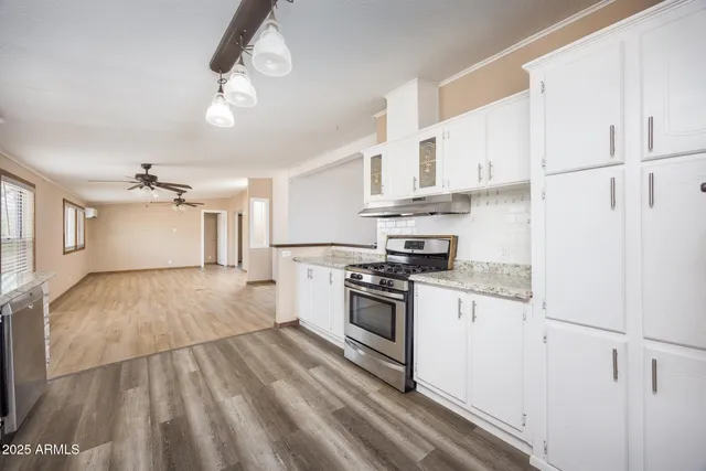 a kitchen with stainless steel appliances granite countertop a stove a refrigerator and white cabinets with wooden floor