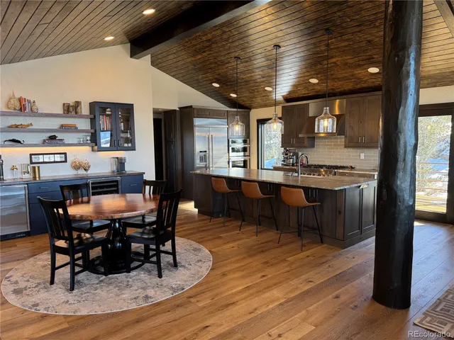 a dining hall with stainless steel appliances kitchen island granite countertop a table chairs and a wooden floor