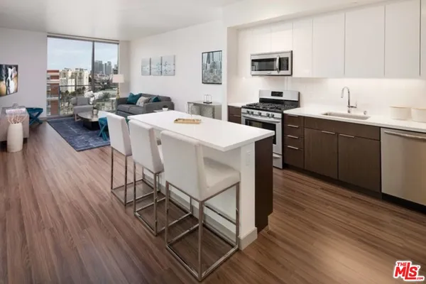 a kitchen with stainless steel appliances kitchen island granite countertop a sink dishwasher a stove a dining table and chairs with wooden floor