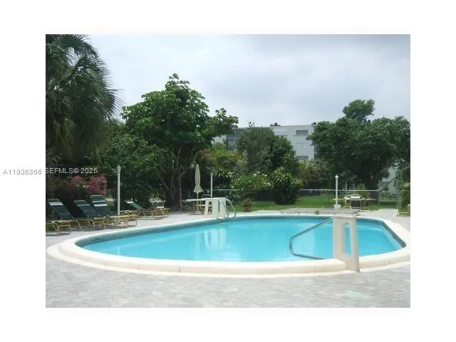 a view of swimming pool with table and chairs under an umbrella with large trees