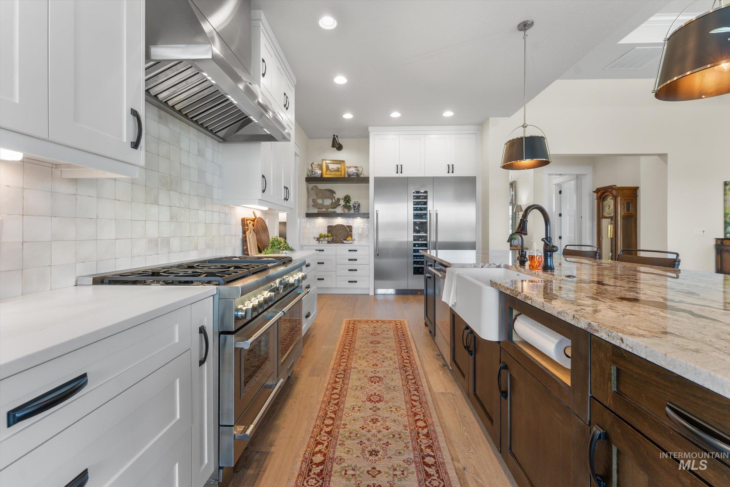 6585 South Pemberley Way Meridian, ID 83642 - Photo 14 of 43 Gourmet kitchen featuring a professional-grade stainless steel range, white shaker cabinetry, tiled backsplash, large center island with a farmhouse sink, and light wood-finish flooring
